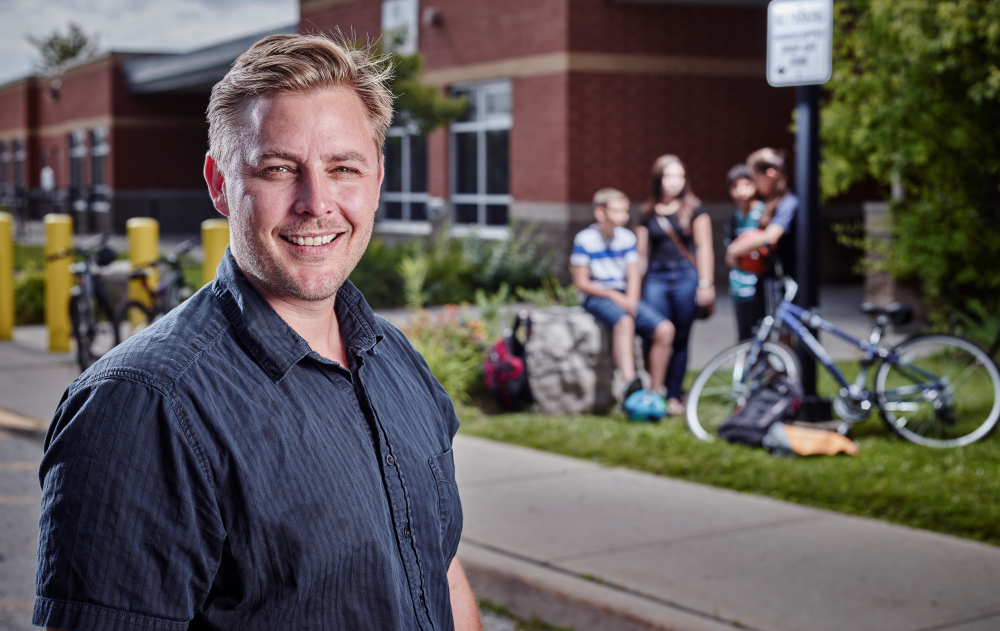 Scott Leatherdale, chercheur principal du COMPASS, un homme blanc se tenant à l'extérieur devant une école et un groupe de quatre élèves, dont deux à vélo, qui discutent.