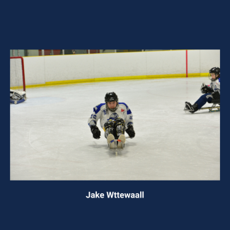 Disability at the Forefront panelist Jake Wttewaall playing sledge hockey. He is skating directly towards the camera, wearing a white jersey and a black helmet.