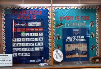 A display at Bruce Trail Public High School that proclaims “Sport is for Everyone”. Large letters cut out of red and reflective silver construction paper make up the words. Surrounding the poster are photographs of students performing various sports. 